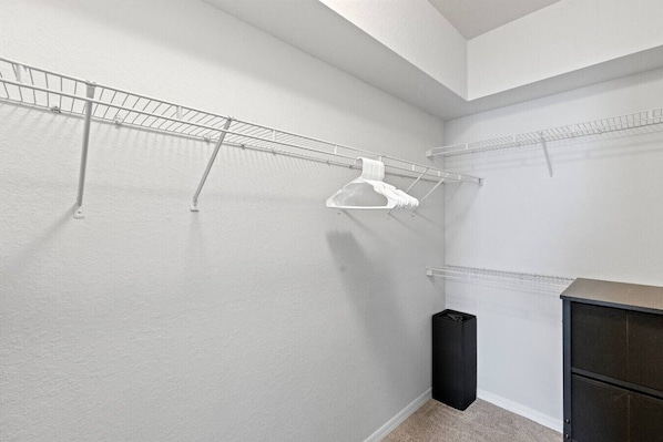 A walk-in closet with metal shelving units, a black trash bin, and a dark-colored cabinet.