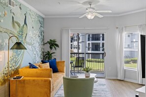 Ein Wohnzimmer mit einer Couch, einem grünen Sessel, einer Stehlampe und einem Wandgemälde.
