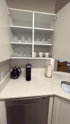 Et køkken med hvide skabe, kaffemaskine, elkedel og vask.