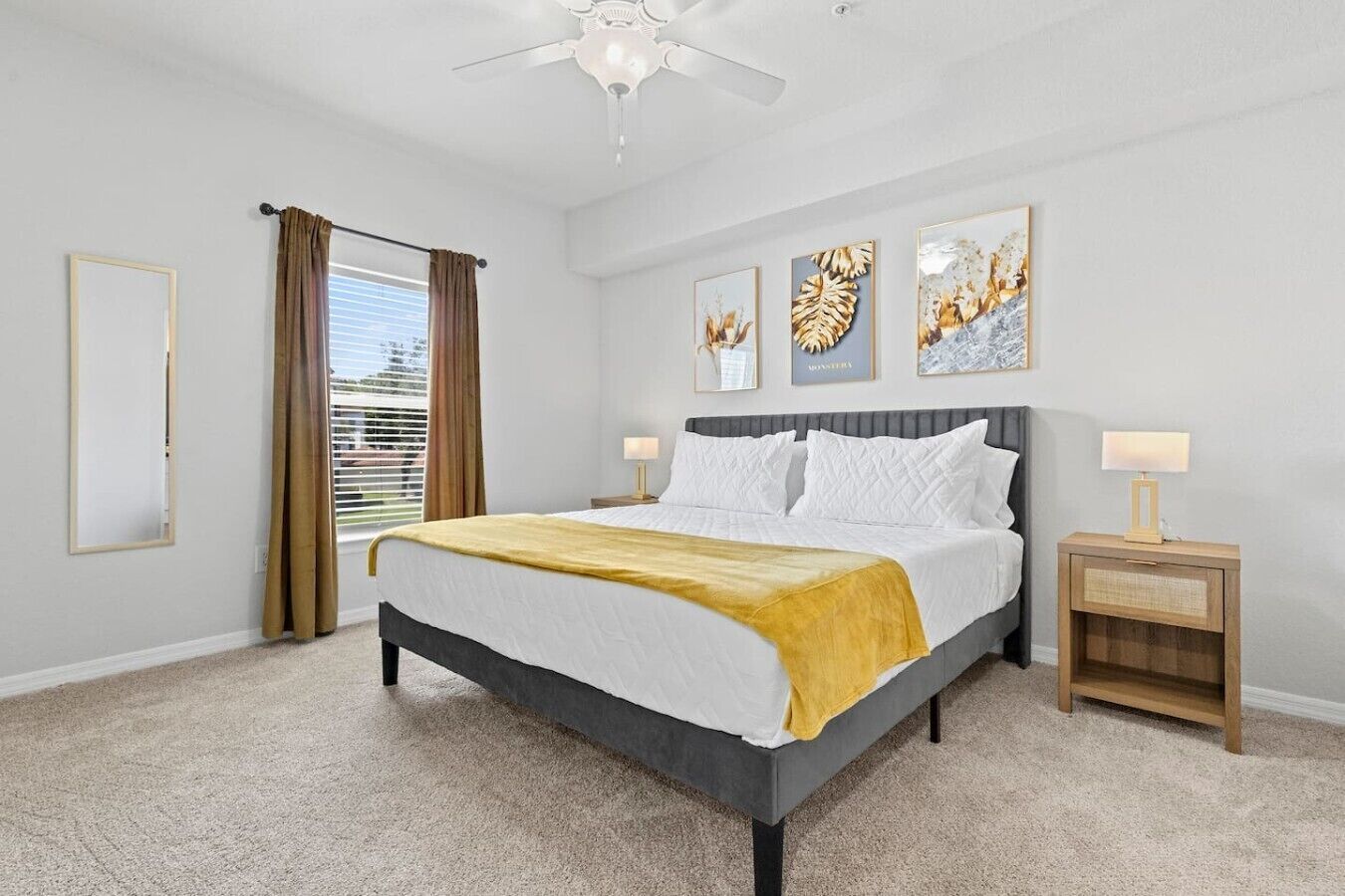 A hotel room with a bed, two bedside tables, a ceiling fan, and artwork on the walls.