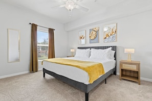 A hotel room with a bed, two bedside tables, a ceiling fan, and artwork on the walls.