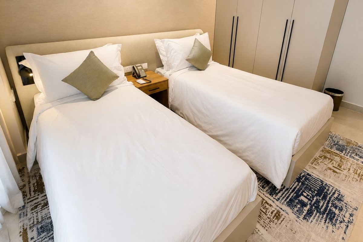 A hotel room with two beds, a cityscape painting on the wall, and a patterned rug.