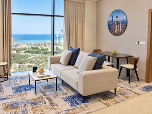 A modern living room with a large window, a sofa, a coffee table, and a dining area. - Citadines Sharq Kuwait (Kuwait City)