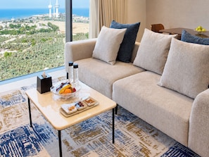 A modern living room with a sofa, a coffee table with snacks, and a view of a cityscape and ocean. - Citadines Sharq Kuwait (Kuwait City)