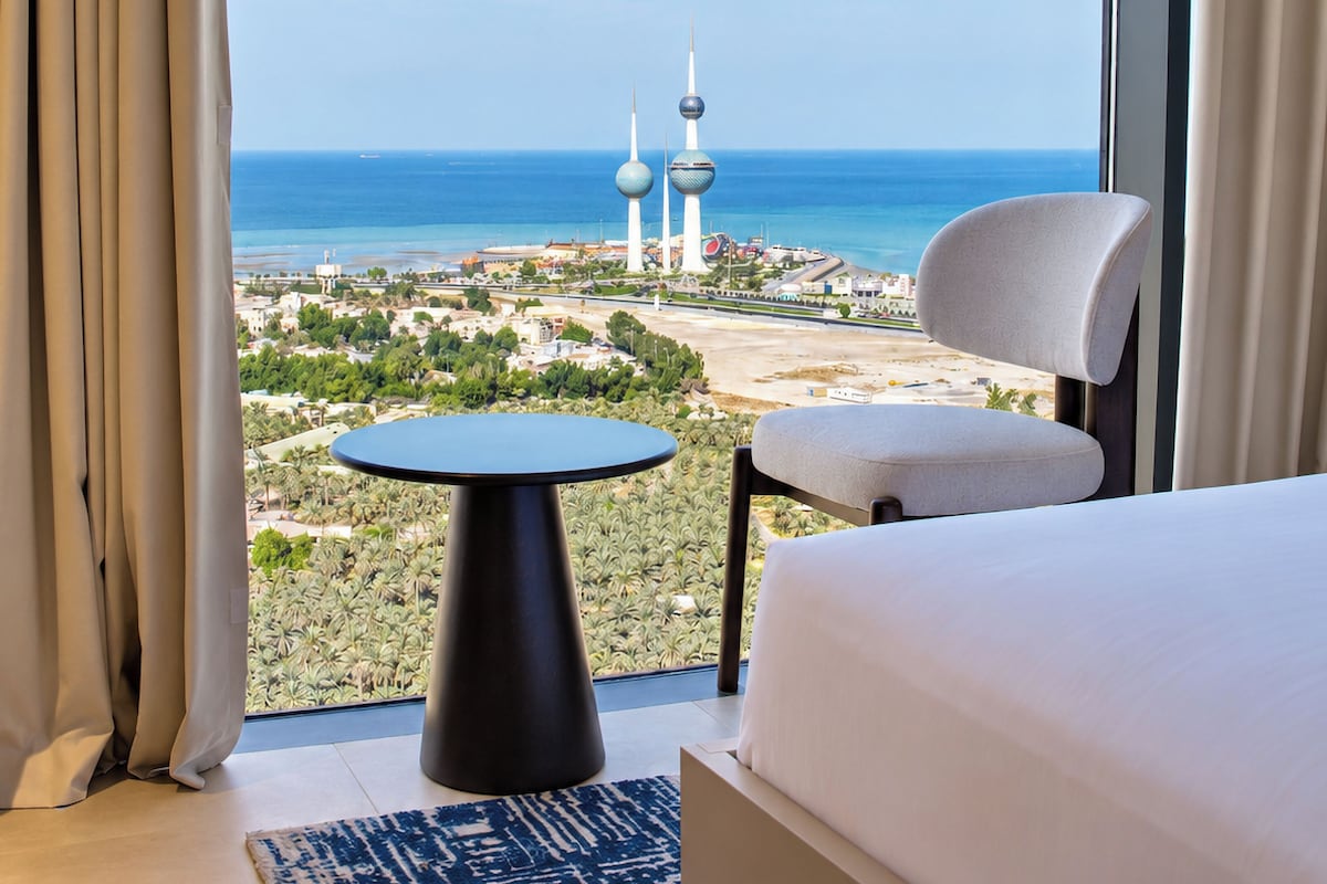 A hotel room with a large window, a bed, a chair, and a small table.