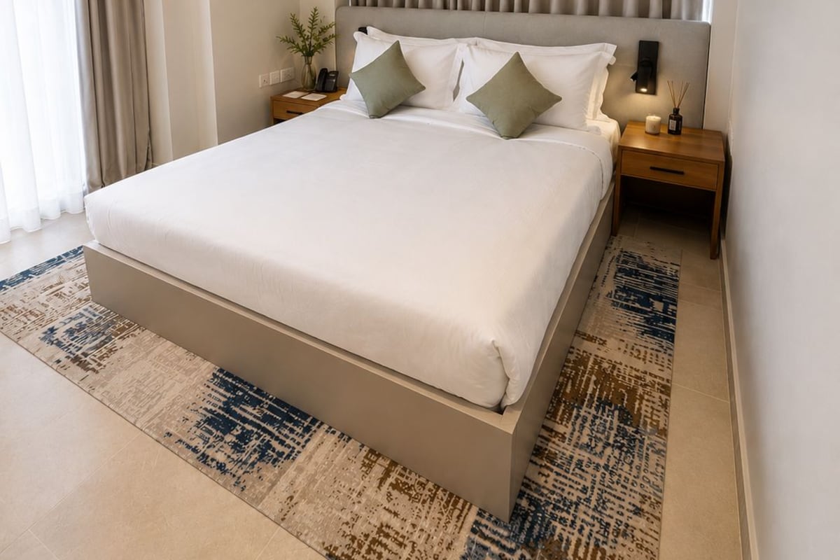 A modern hotel room with a large bed, a nightstand, a wall-mounted lamp, and a window with curtains.