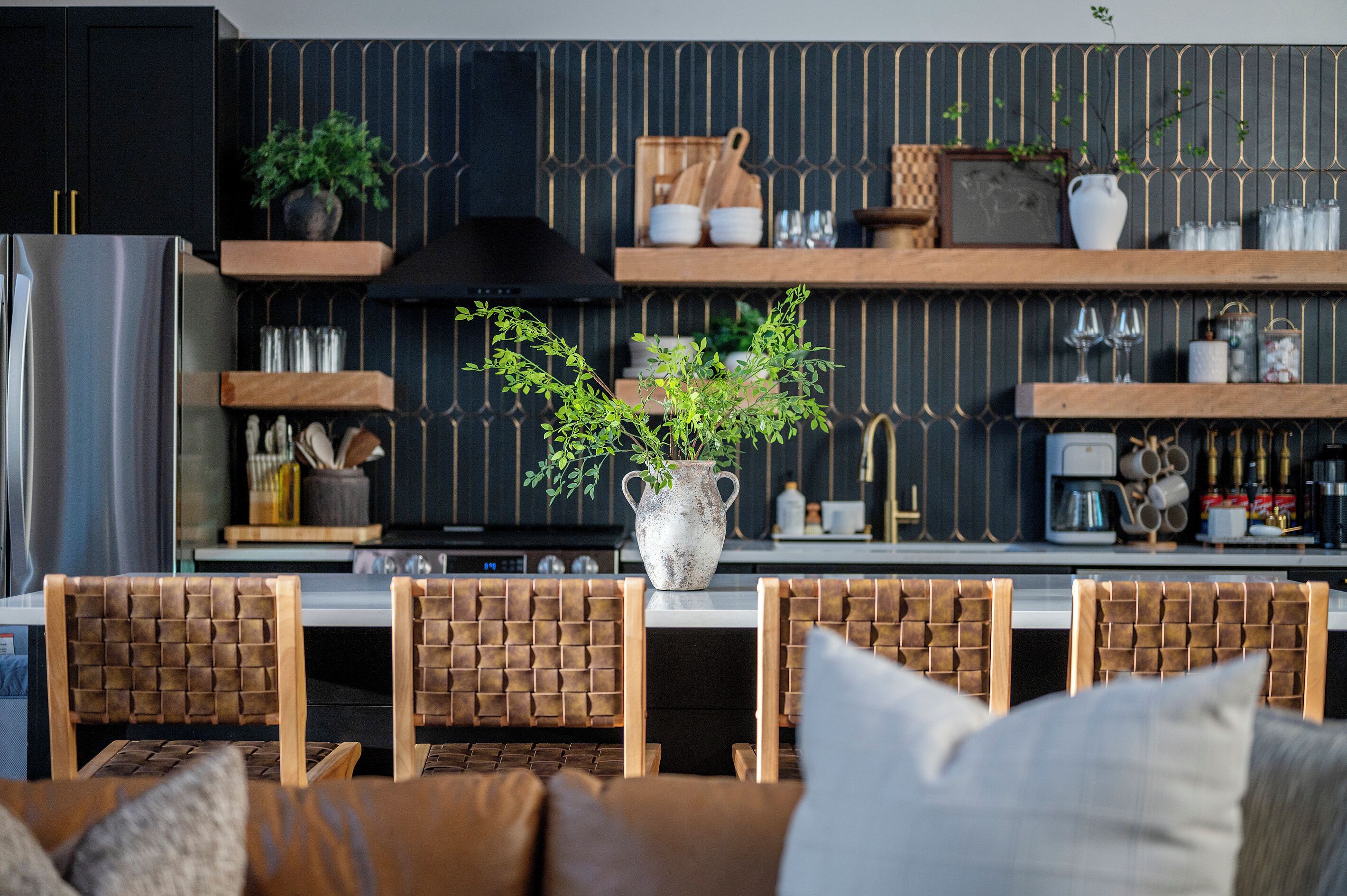 Una cocina moderna con una isla central, sillas de madera, una planta en maceta y utensilios de cocina en estantes.