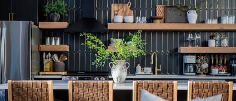 Une cuisine moderne avec un îlot central, des chaises en bois, une plante en pot et des ustensiles de cuisine rangés sur des étagères.