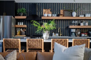 Une cuisine moderne avec un îlot central, des chaises en bois, une plante en pot et des ustensiles de cuisine rangés sur des étagères.