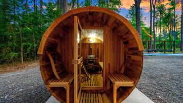 Una estructura de sauna de madera con bancos y una mesa, rodeada por un bosque.