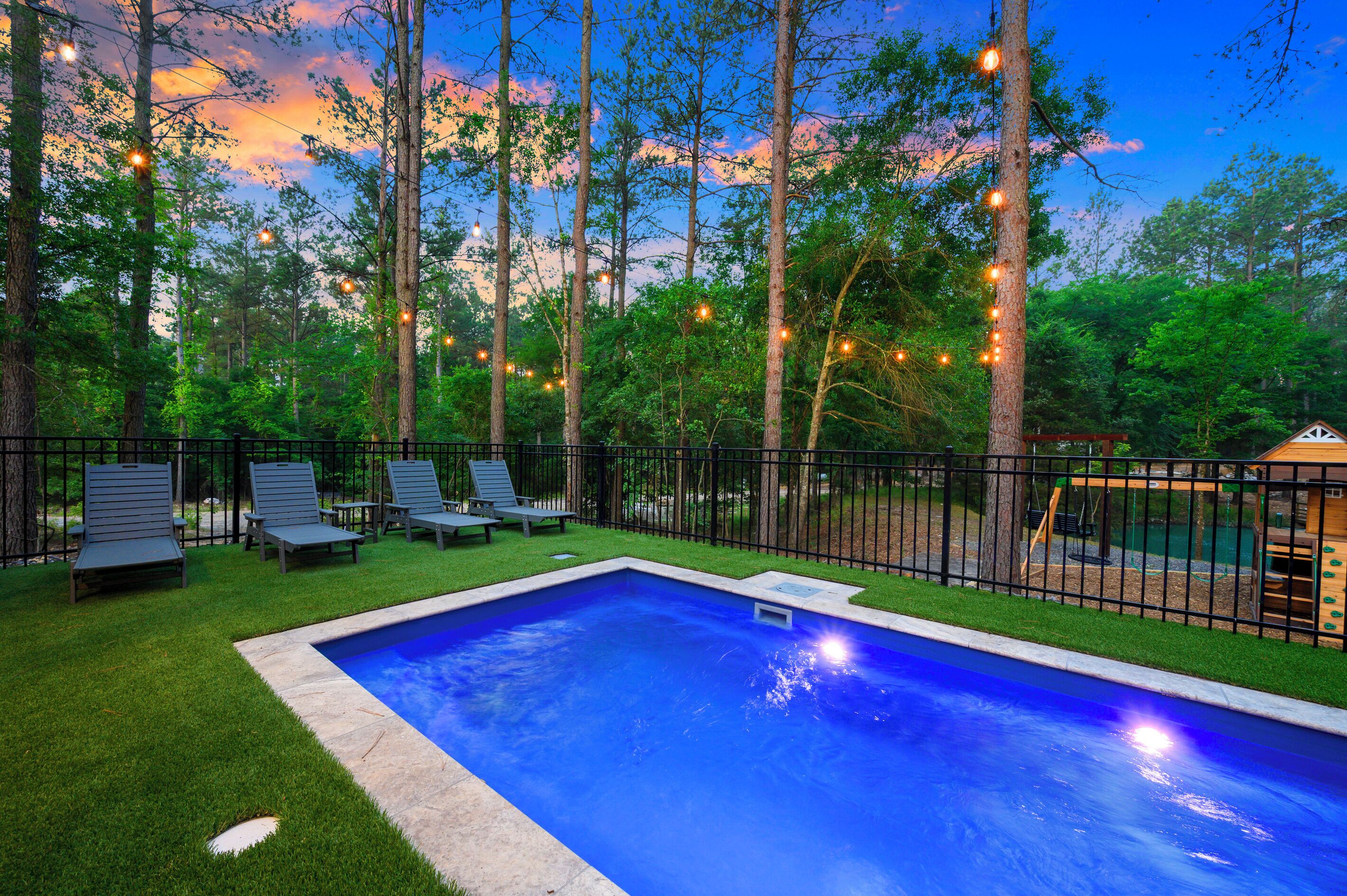 Una piscina con un área verde circundante, una terraza de madera y un parque infantil.