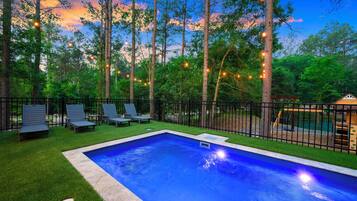 Una piscina con un área verde circundante, una terraza de madera y un parque infantil.