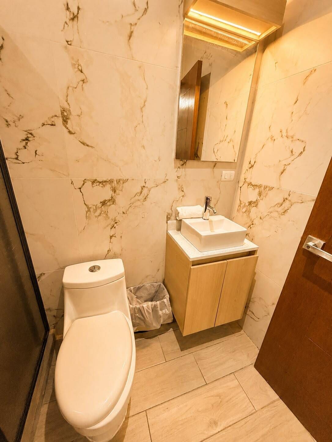 A bathroom with a toilet, sink, mirror, and marble walls.