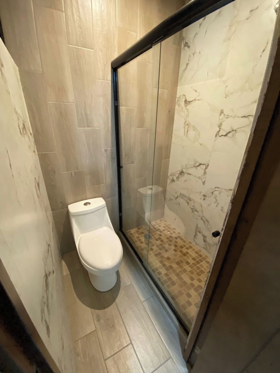A bathroom with a toilet, a glass shower enclosure, and tiled flooring.