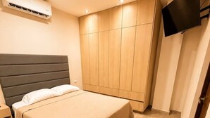 A bedroom with a bed, a wardrobe, a television, and an air conditioning unit.