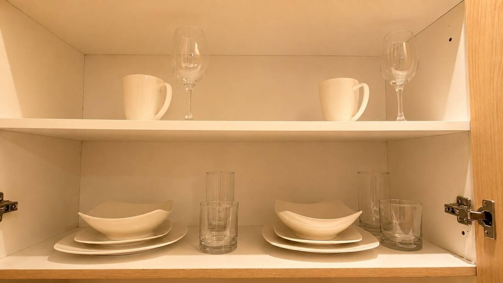 A shelf with white dinnerware and clear glasses.