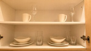 A shelf with white dinnerware and clear glasses.