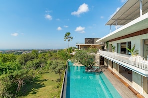 A modern house with a swimming pool, lush greenery, and a clear view of the cityscape.