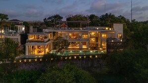 Una casa moderna de varios pisos con una piscina, rodeada de abundante vegetación.