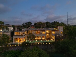 A multi-story modern house with a swimming pool, surrounded by lush greenery.