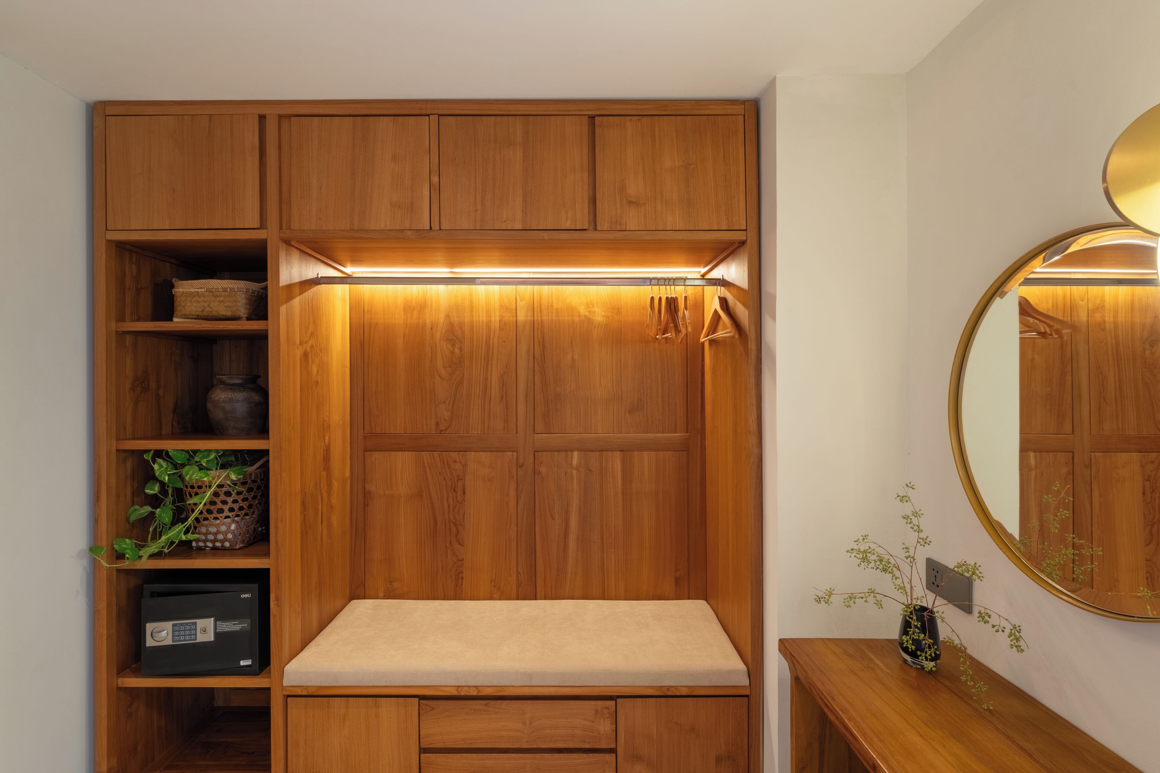 A wooden wardrobe with a mirror, a shelf with decorative items, and a bedside table with a vase.