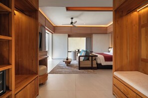 A modern hotel room with a wooden floor, a bed, a sofa, a TV, and a ceiling fan.