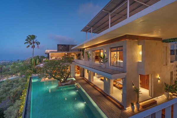 A modern hotel with a large pool, multiple balconies, and a view of the surrounding landscape.