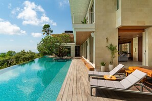 A modern infinity pool with a wooden deck, lounge chairs, and potted plants.