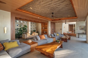 A spacious living area with a modern design, featuring a large sofa set, wooden coffee tables, and a ceiling with a unique pattern.