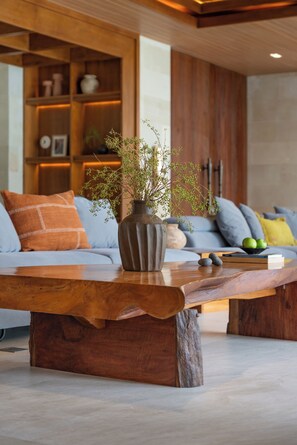 A modern living room with a wooden coffee table, a sofa with cushions, and a vase with branches.