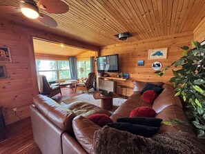 A cozy cabin interior with a leather sofa, a television, and wooden walls.
