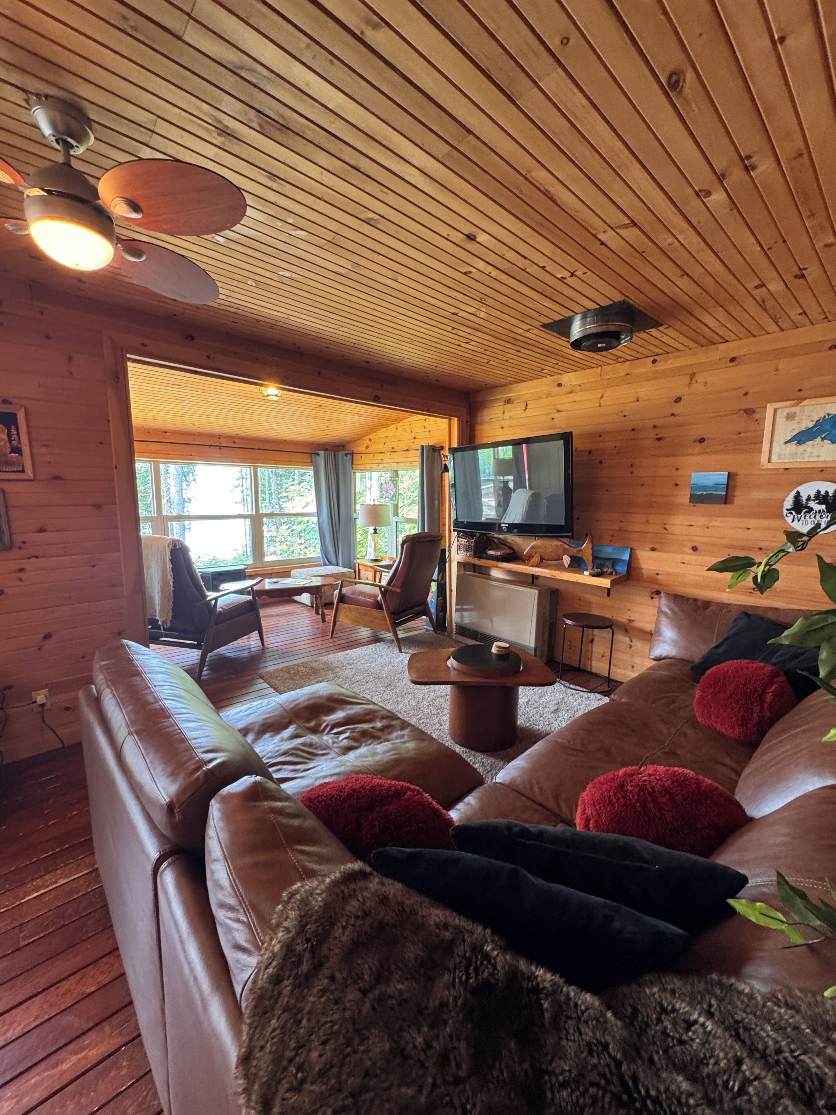 L’intérieur chaleureux d’un chalet avec un canapé en cuir, un téléviseur et un plafond en bois.