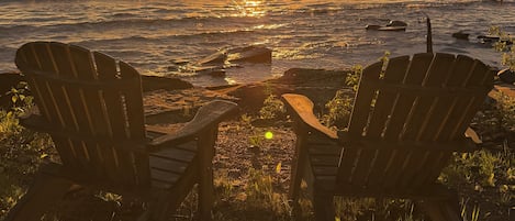 Dos sillas Adirondack de madera mirando al atardecer sobre un cuerpo de agua.