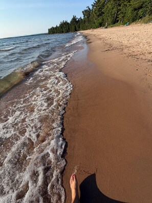 A sandy beach with gentle waves and a forested area in the background.