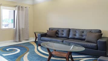 A living room with a dark leather sofa, a glass coffee table, and a blue patterned rug.