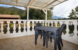 Eine überdachte Terrasse mit Tisch und Stühlen, ein weißes Geländer und Blick auf Berge.