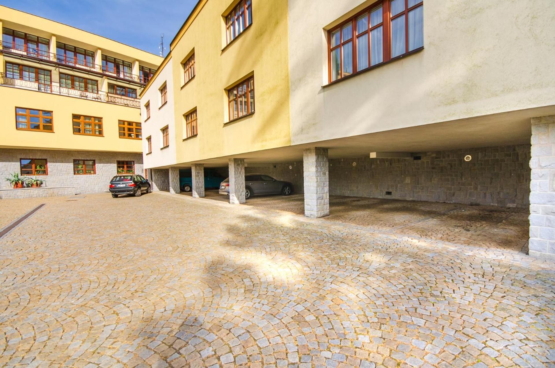 A building with multiple floors, a courtyard with cobblestone paving, and several parked cars.