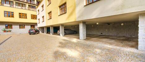 A building with multiple floors, a courtyard with cobblestone paving, and several parked cars.