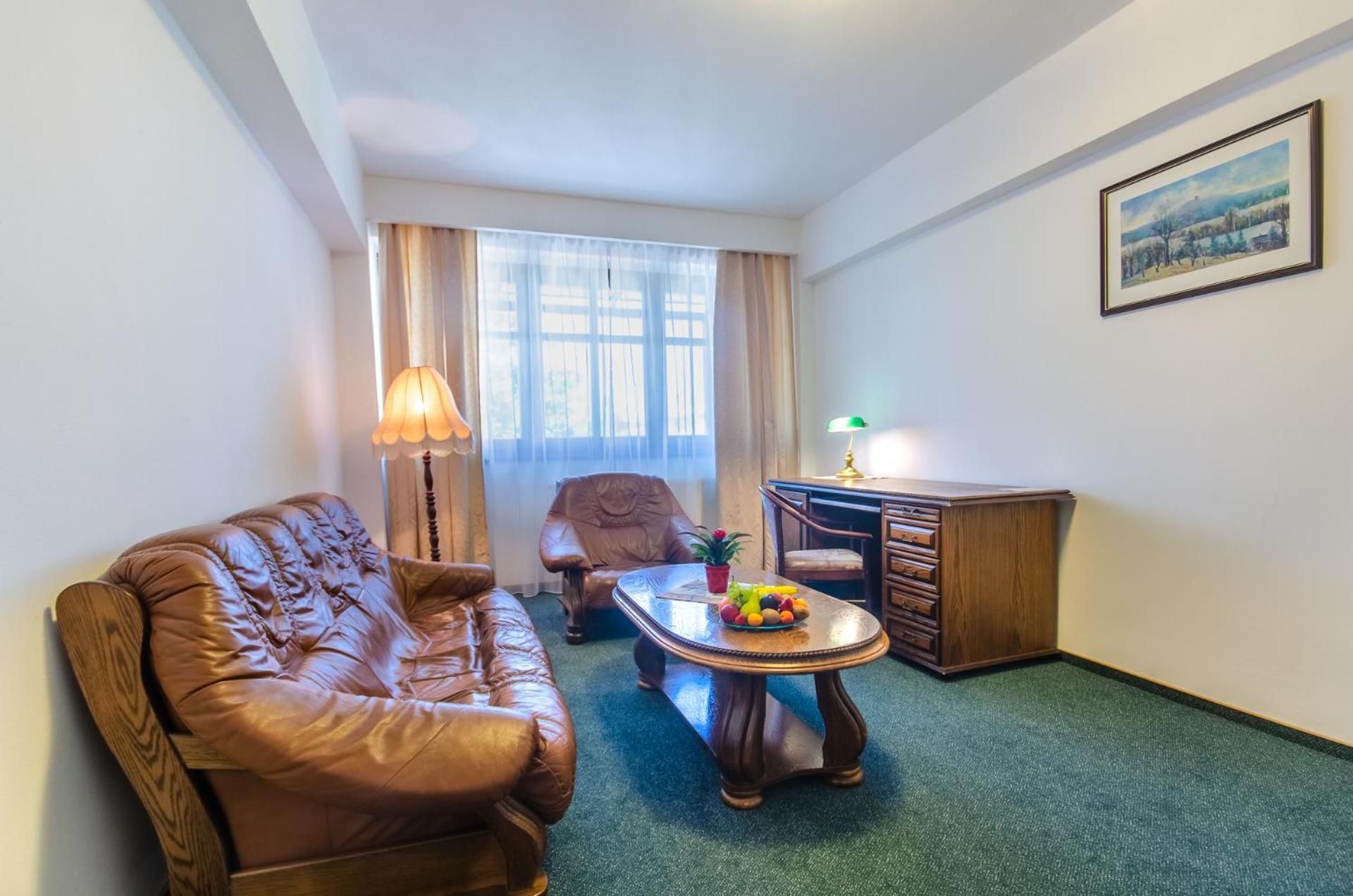 A room with a leather sofa, a wooden desk, a small table with fruit, and a painting on the wall.