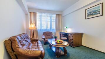 A room with a leather sofa, a wooden desk, a small table with fruit, and a painting on the wall.