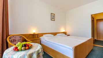 A hotel room with a single bed, bedside tables, a chair, and a small table with fruit.