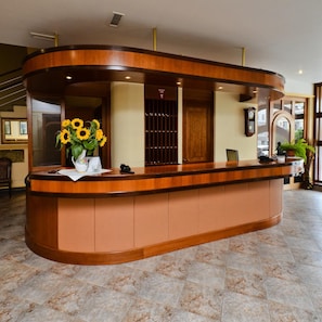 A reception desk with a curved design, a vase of sunflowers, a clock, and a potted plant.