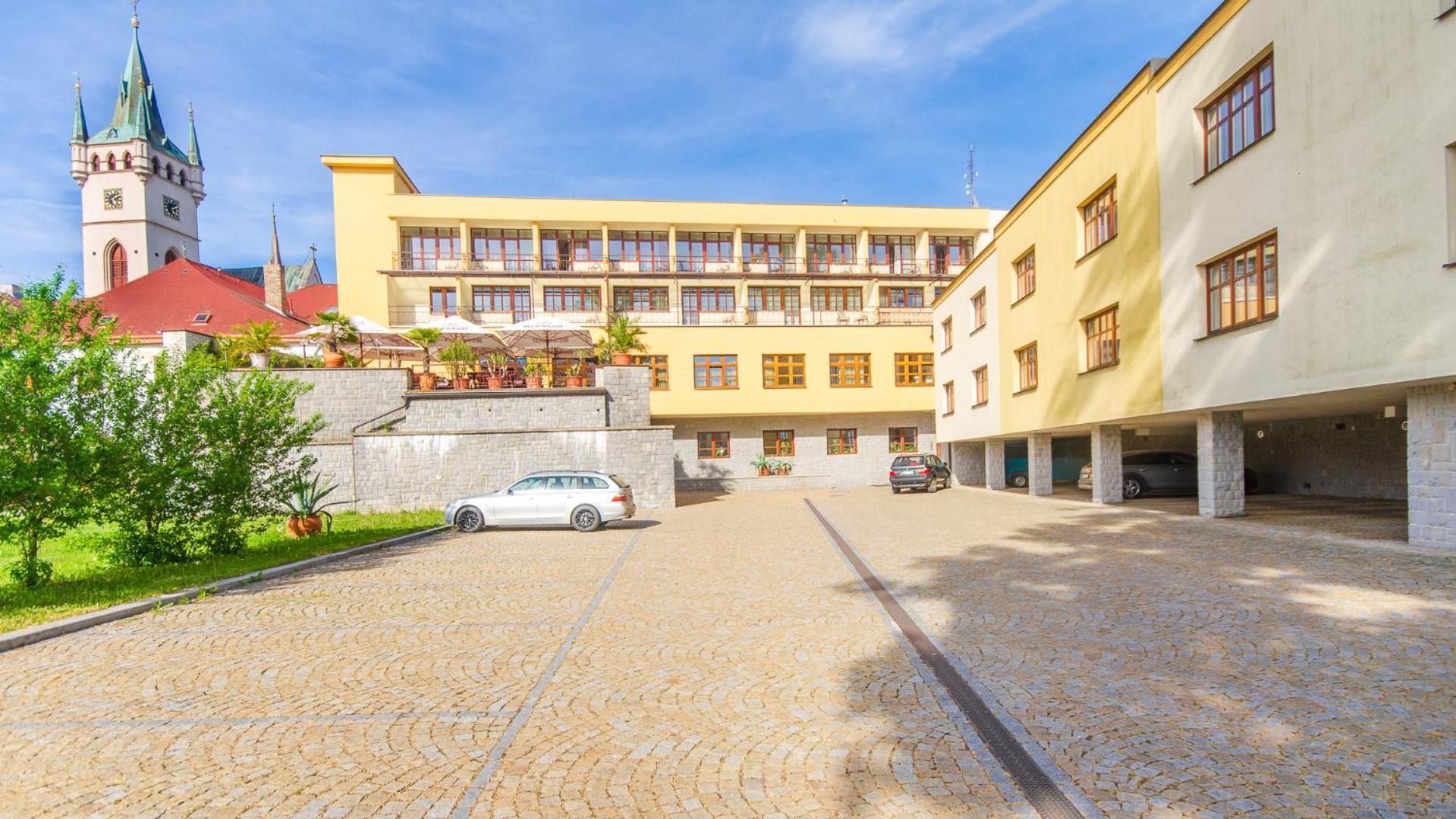 A courtyard with cobblestone pavement, a white car, and a building with multiple windows and balconies.