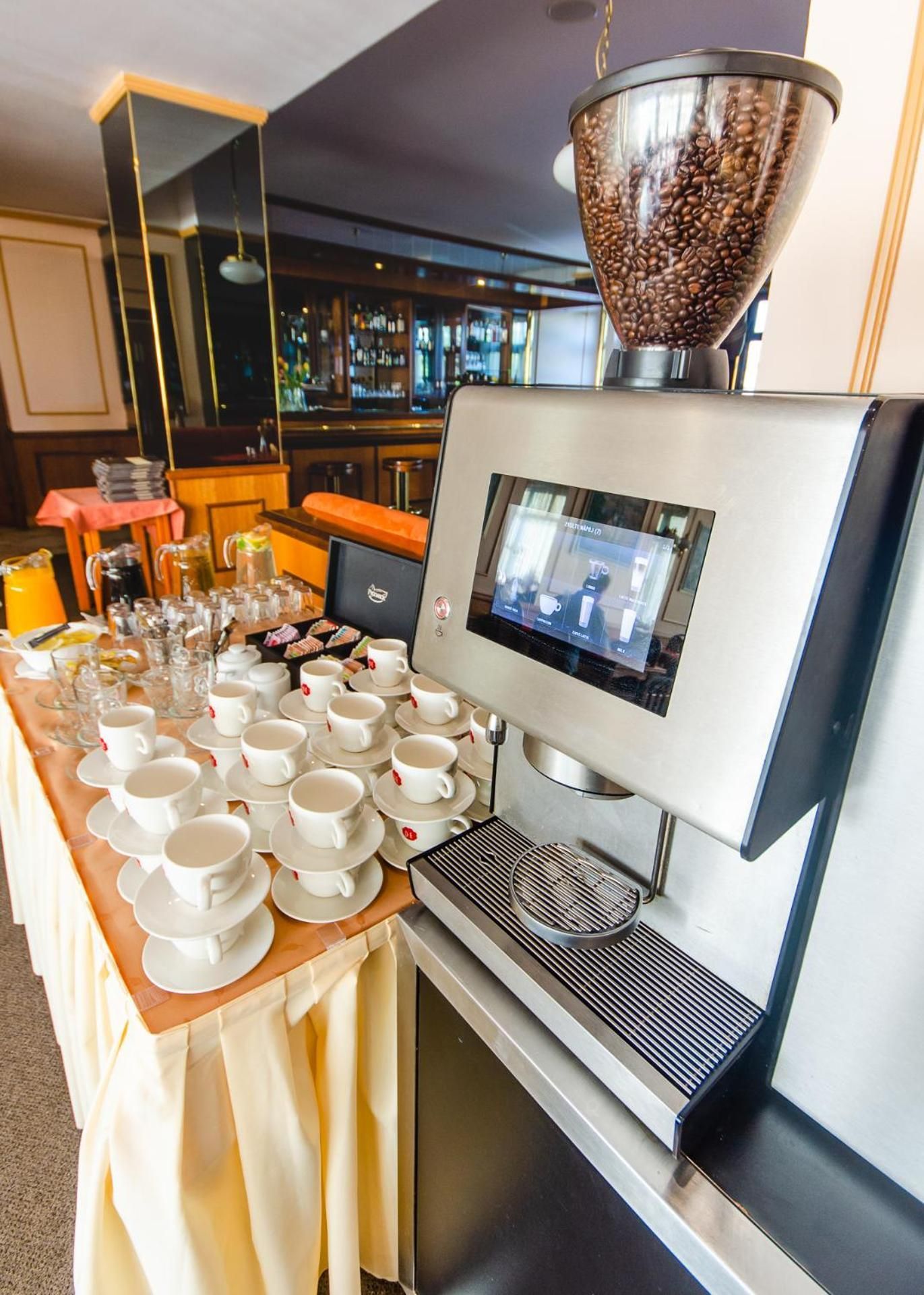 A coffee machine with a digital display, a coffee grinder, and a tray of white cups and saucers.