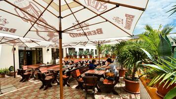 An outdoor seating area with tables and chairs under umbrellas, surrounded by potted plants.