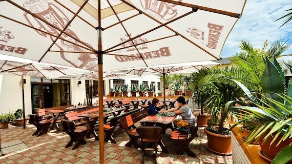 An outdoor seating area with tables and chairs under umbrellas, surrounded by potted plants.