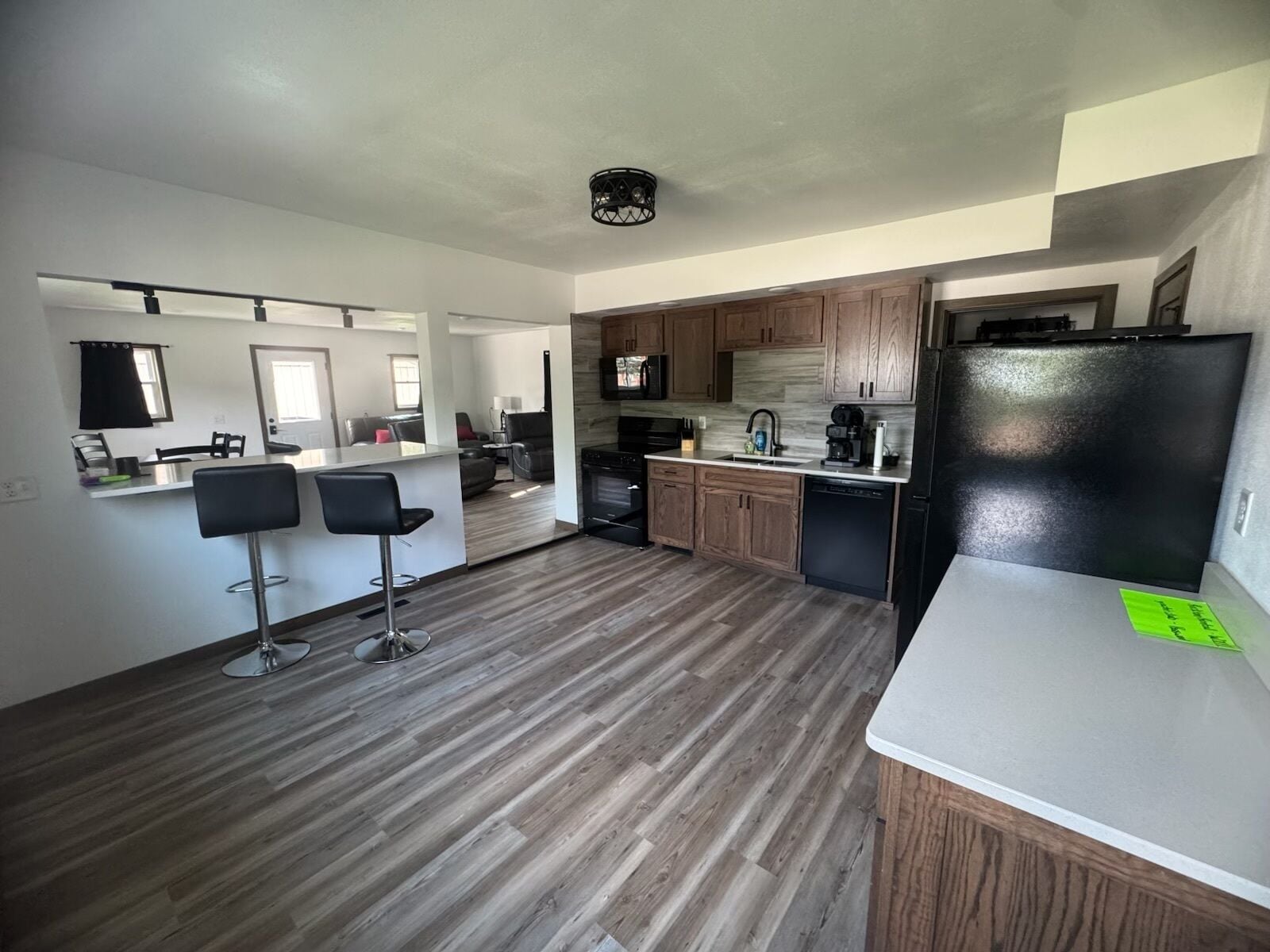 A modern kitchen with a central island, bar stools, wooden cabinets, and a black refrigerator.