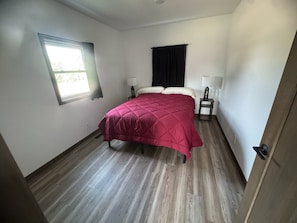 A bedroom with a bed, two bedside tables with lamps, a window with curtains, and a door. - New spacious house, 3 bedroom next to Rockton Bar and Kickapoo (La Farge)