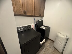 A laundry room with a front-loading washer and dryer, wooden cabinets above, and a white mattress on the floor. - New spacious house, 3 bedroom next to Rockton Bar and Kickapoo (La Farge)