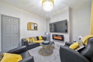 Ein modernes Wohnzimmer mit einer grauen Tür, einem schwarzen Ledersofa, einem runden Couchtisch und einem flachbildfernseher, der an der Wand angebracht ist.